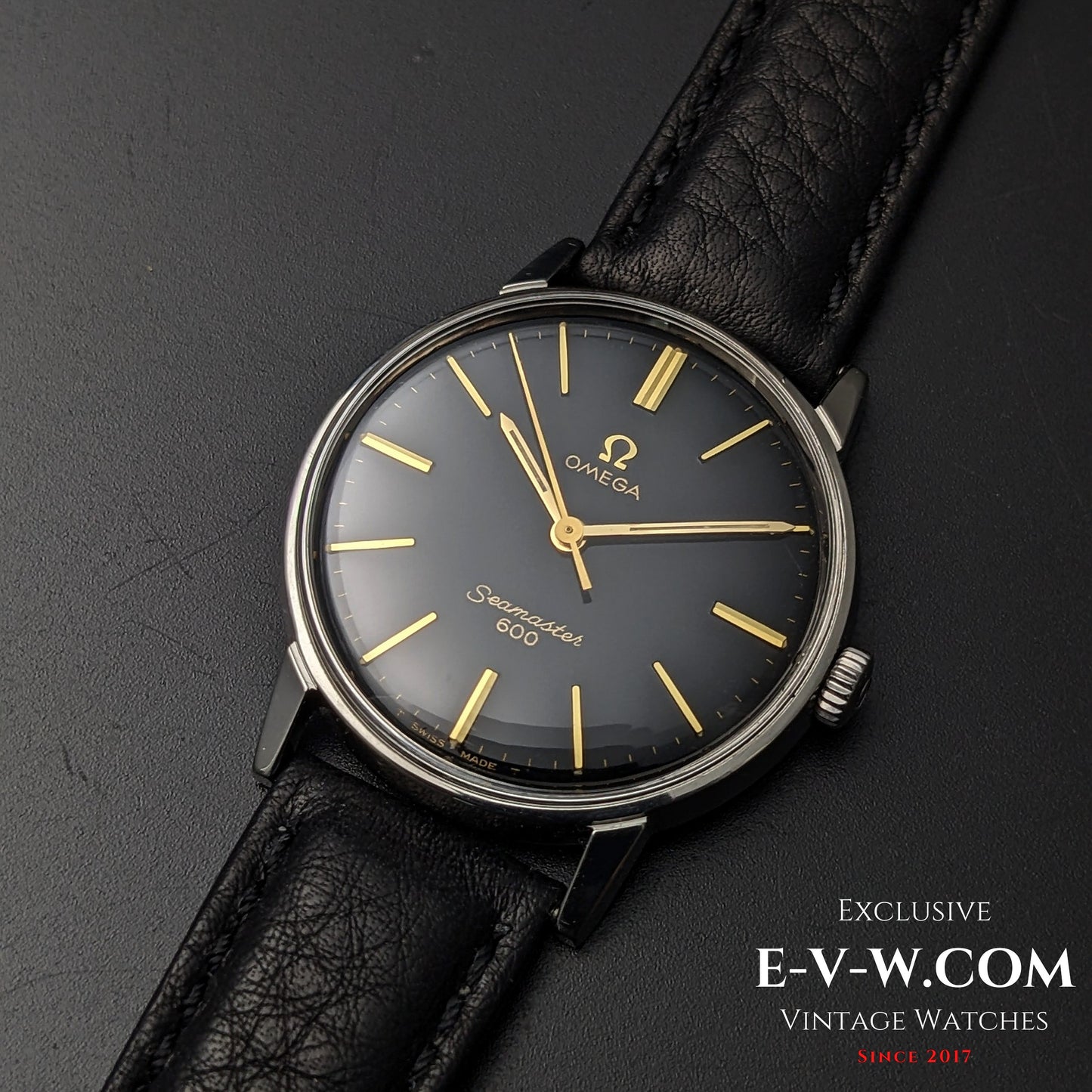 Front view of 1966 Omega Seamaster 600 Ref. 135011 with black dial and gold markers, paired with a black leather strap on dark background.