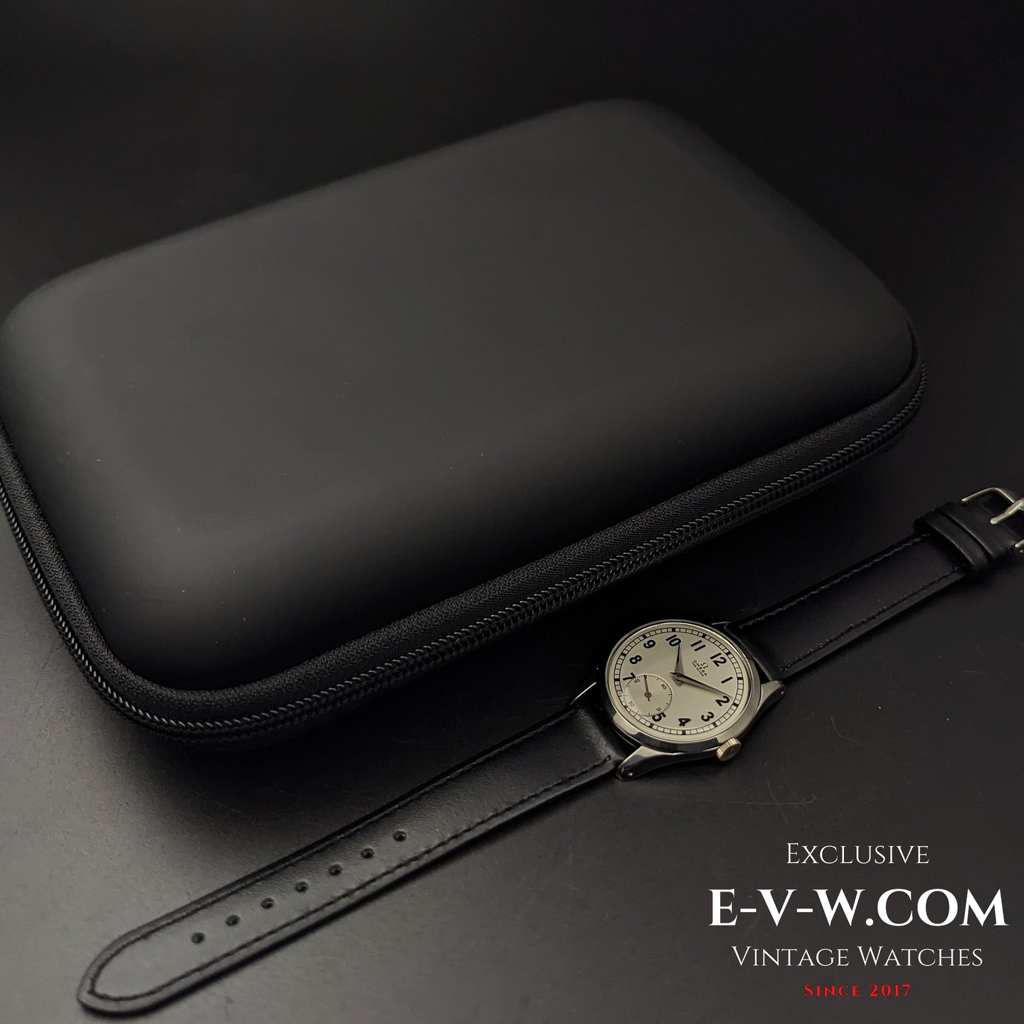 Omega FAB SUISSE Ref. 2750-6 vintage wristwatch displayed next to a black protective case. A 1954 classic with a silver dial and black leather strap.