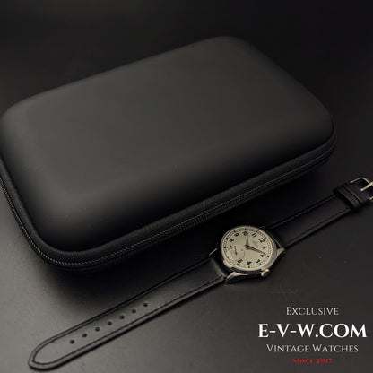 Omega FAB SUISSE Ref. 2750-6 vintage wristwatch displayed next to a black protective case. A 1954 classic with a silver dial and black leather strap.
