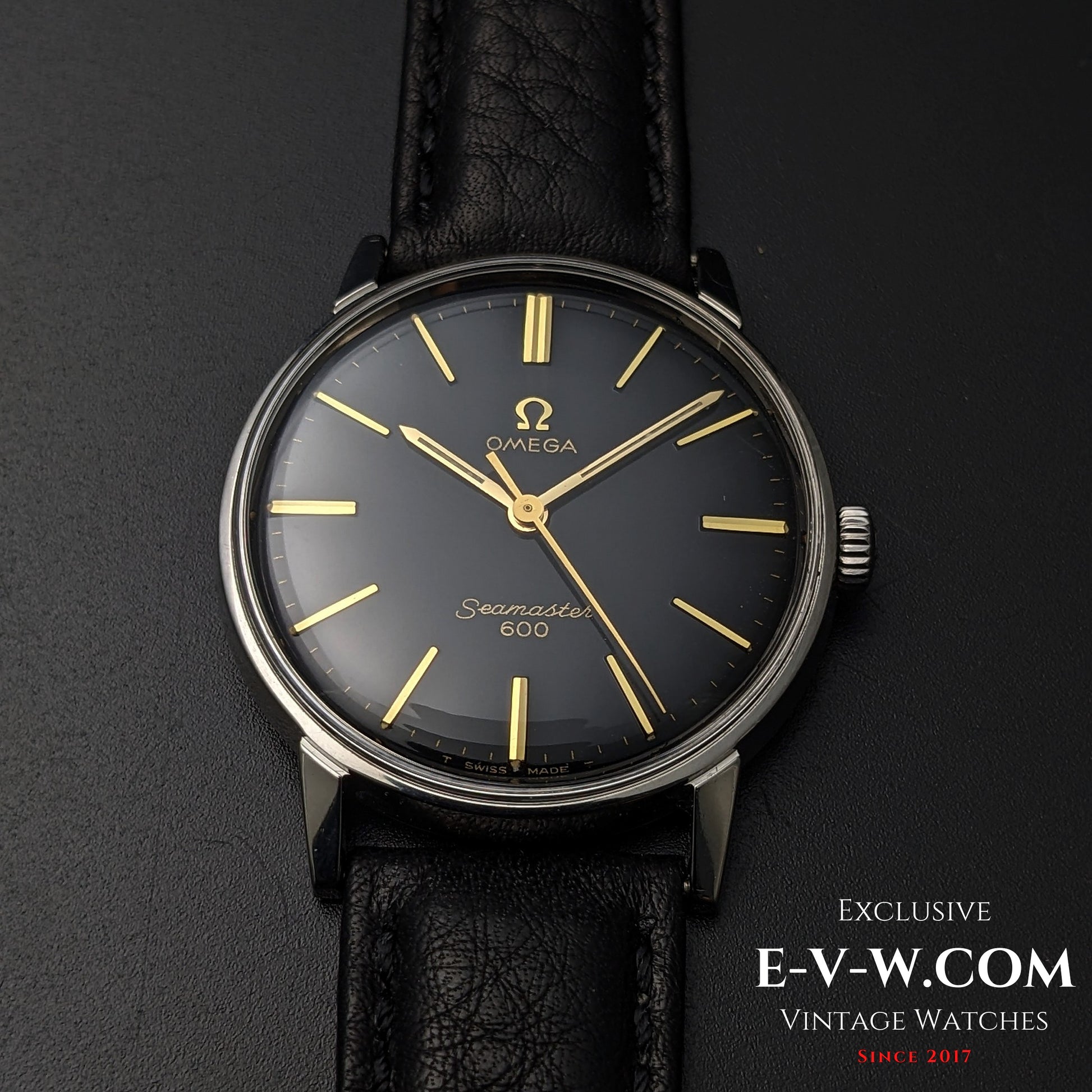 Front-facing view of Vintage Omega Seamaster 600 1966 Ref. 135011 with black dial, gold markers, and black leather strap on dark surface.
